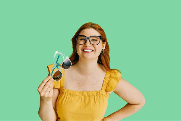 Woman holding 2 pairs of eyeglasses while smiling at the camera