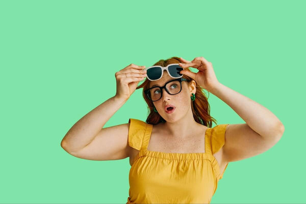 Woman holding a pair of progressive sunglasses while wearing a pair of eyeglasses