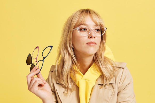 Woman wearing a pair of eyeglasses while holding 2 more pairs in her hand