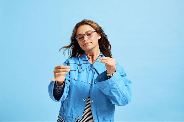 Getting used to new glasses: A woman wears glasses and holds two more frames in front of a blue background.
