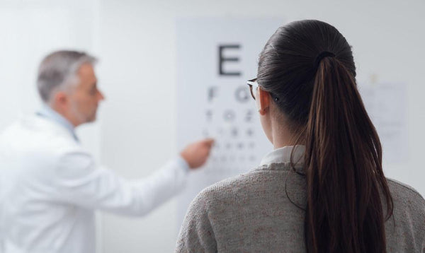 Bifocal vs. progressive: A woman reading an eye chart with a doctor in front of her.