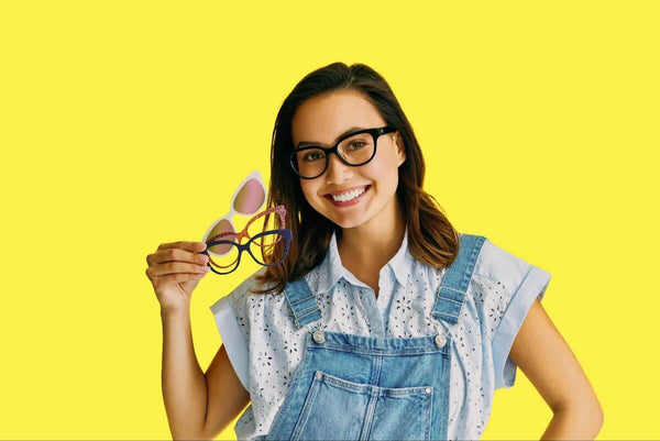 Woman smiling at the camera while holding 3 pairs of eyeglasses