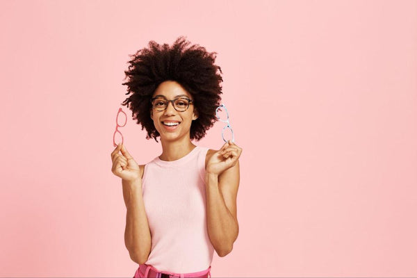 Woman wearing the best glasses for oval faces in front of a pink background.