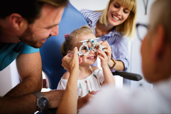 A young girl with her parents smiling during an eye exam.