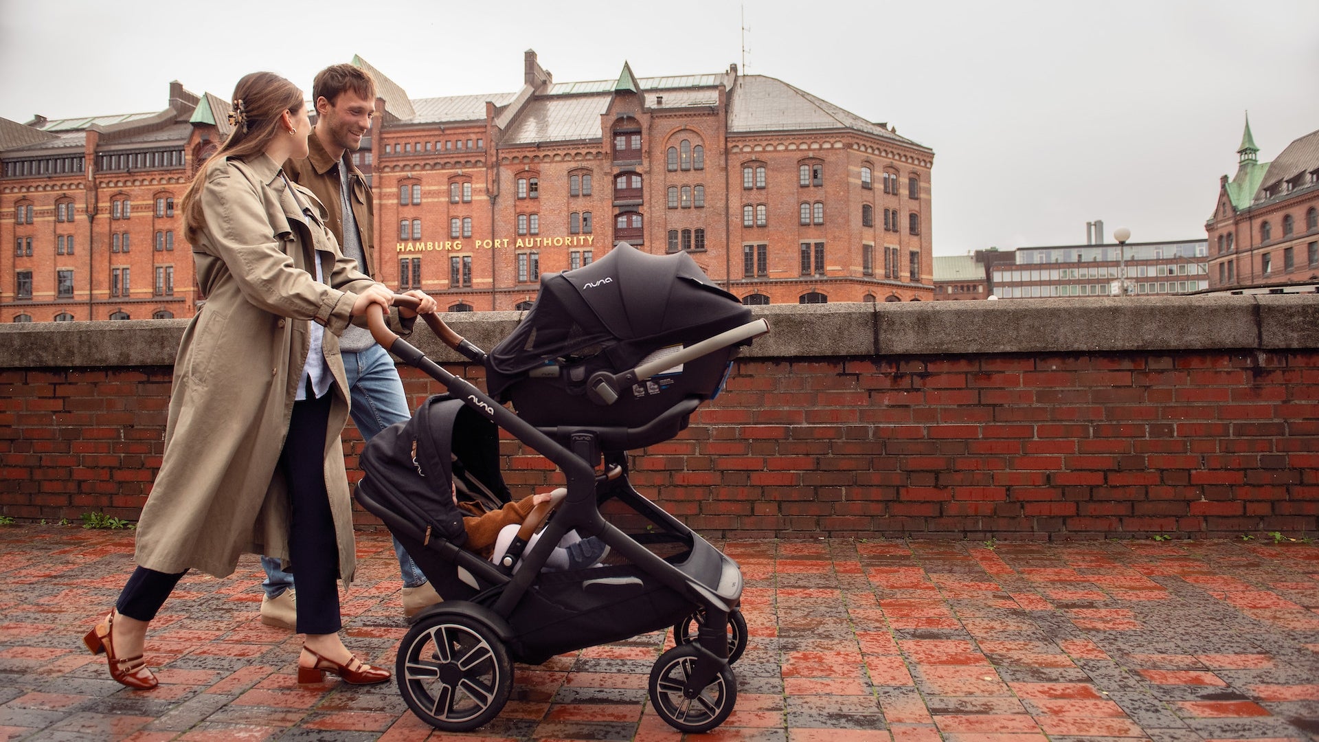 Parents pushing Nuna Demi Next with infant seat on top and toddler on bottom
