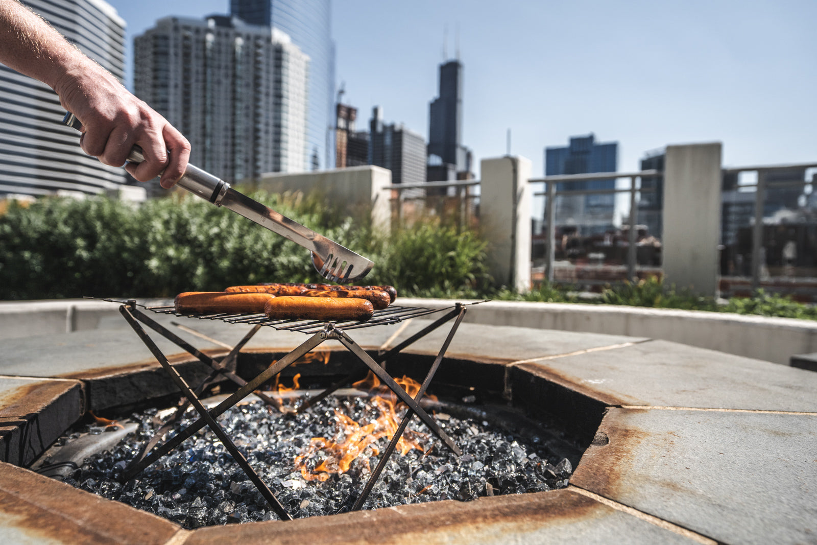Grilling hotdogs over a rooftop fire pit in the city