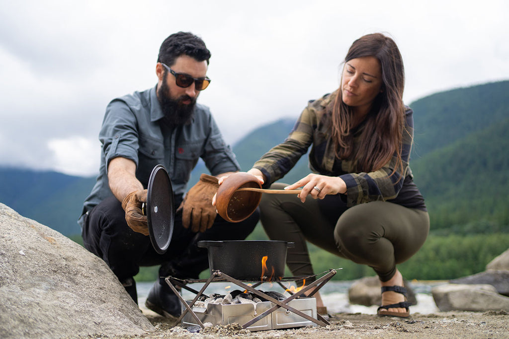 Two People Cooking With Cast-Iron Dutch Oven on Outdoor Campfire