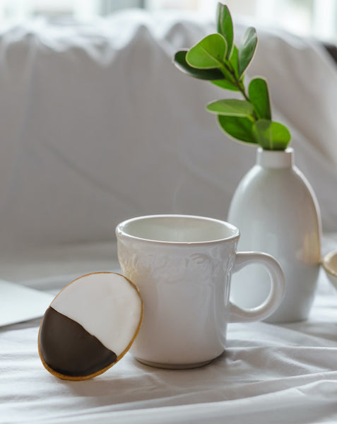 black and white biscuit leaning on white mug with plant behind it