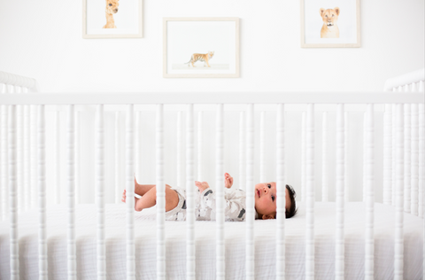 Baby sleeping safely on his back in a crib where all accessories and pillows have been removed for safe sleep
