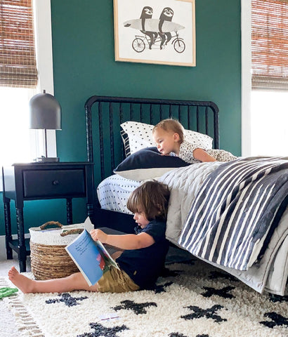 Siblings reading in a dark green room by the DaVinci Jenny Lind Twin Bed in Ebony finish and matching Jenny Lind Spindle Nightstand