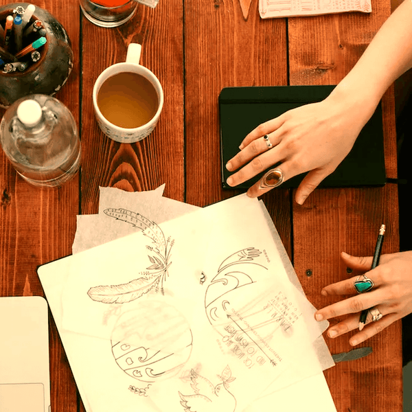 a desktop scene with hands sketching images on paper