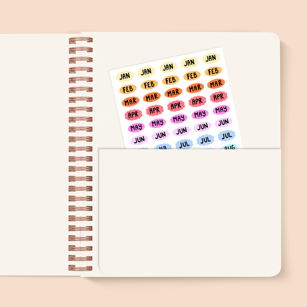 image of a paper pocket inside a planner with a sheet of small multi-colored stickers with the names of the months