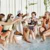 Five women sitting around a pool, celebrating.