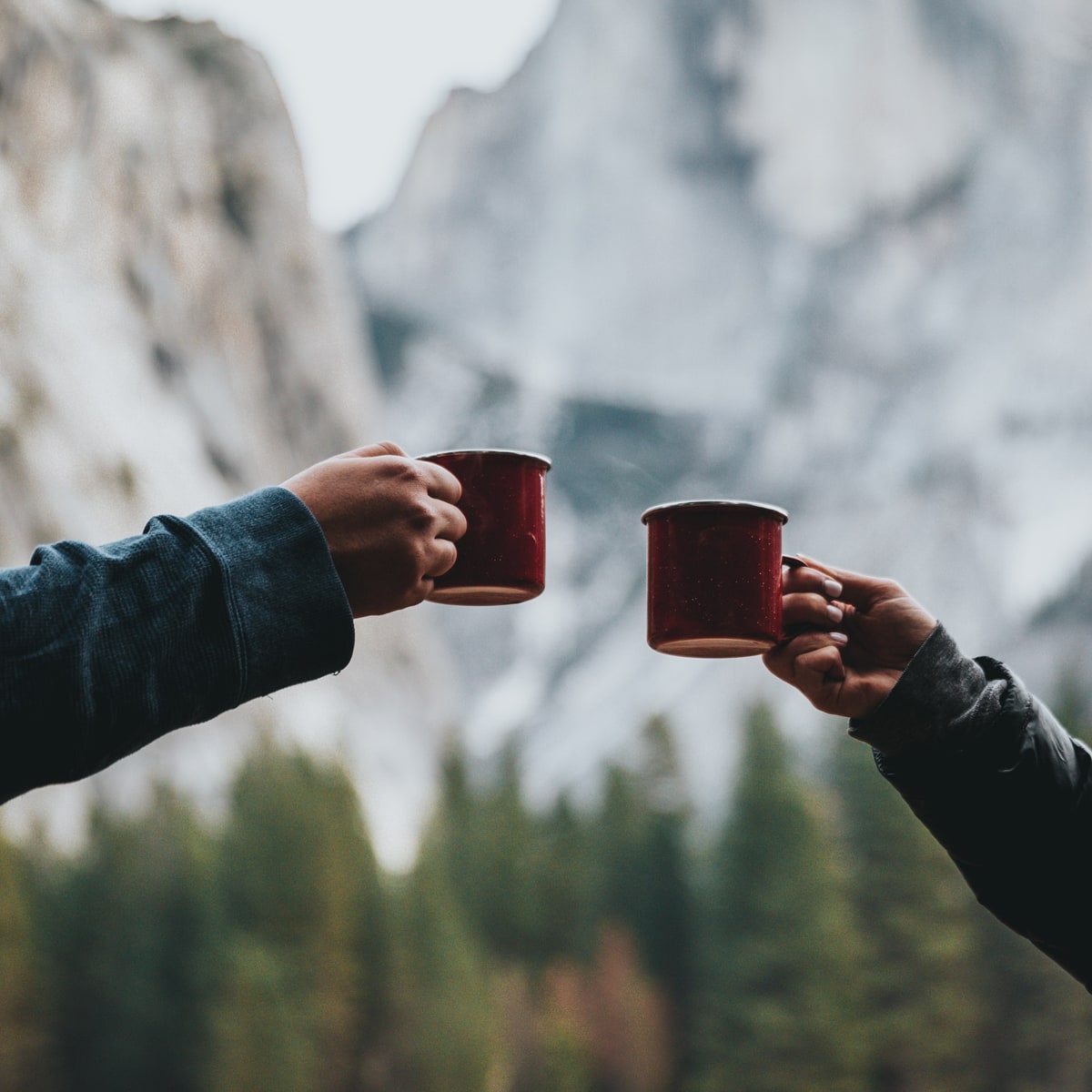 Two people cheers two warm steaming cups of coffee.