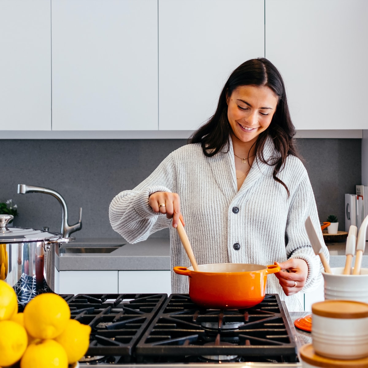 A woman is smiling as she cooks in the kitchen.