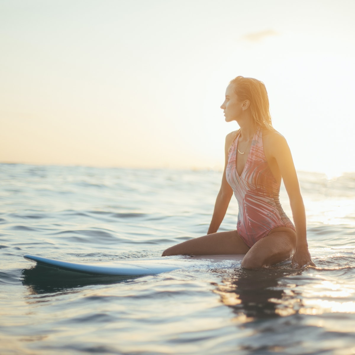 Woman sitting on surfboard in the ocean waiting for a wave to catch.