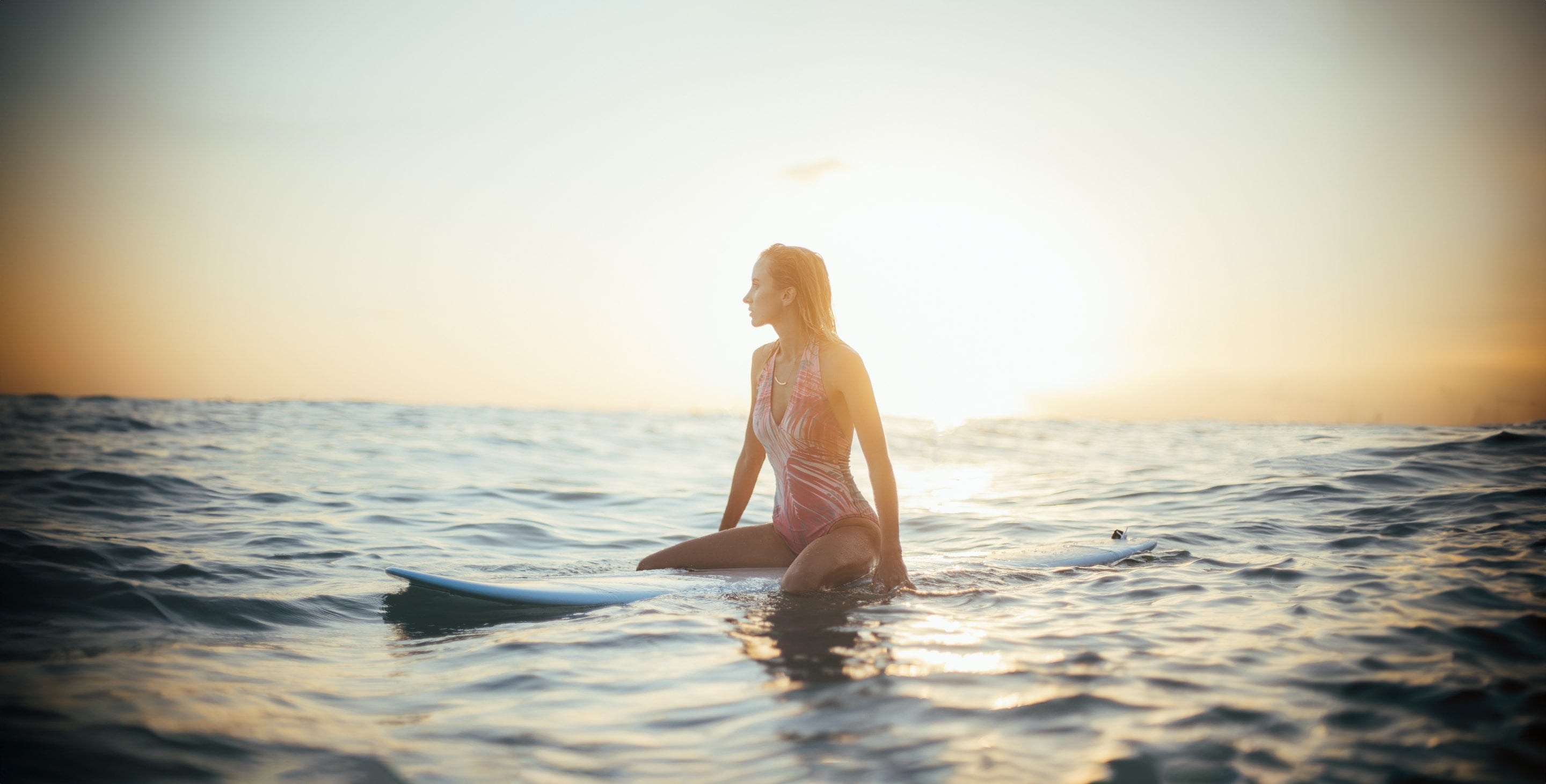 Woman sitting on surfboard in the ocean waiting for a wave to catch.