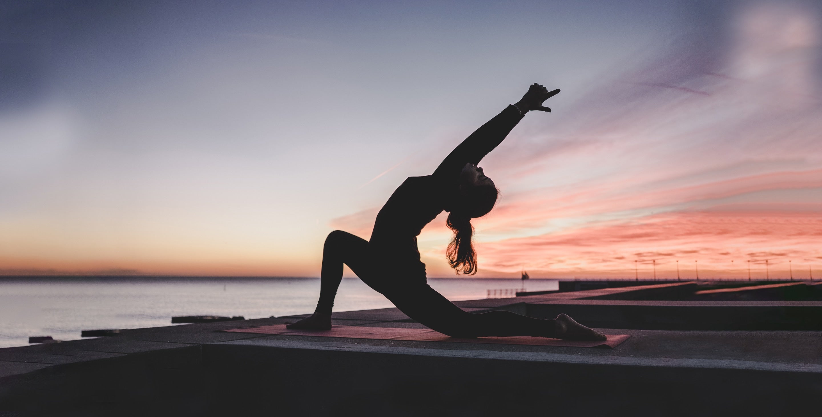 A woman is doing sunset yoga on a lake dock.