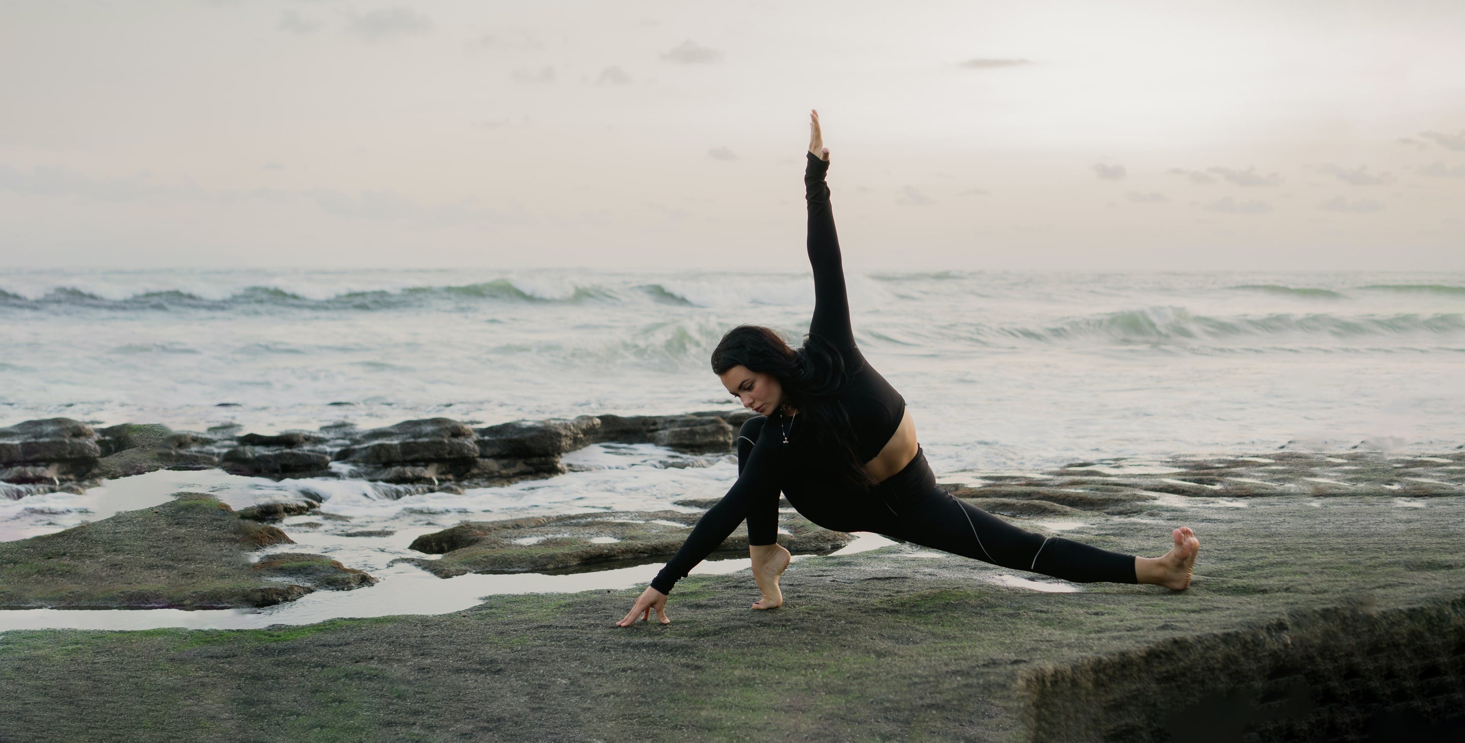 A woman doing yoga on rocks near the ocean.