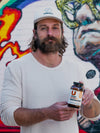 Christopher Walker holding a bottle of Redwood standing in front of a graffiti wall.