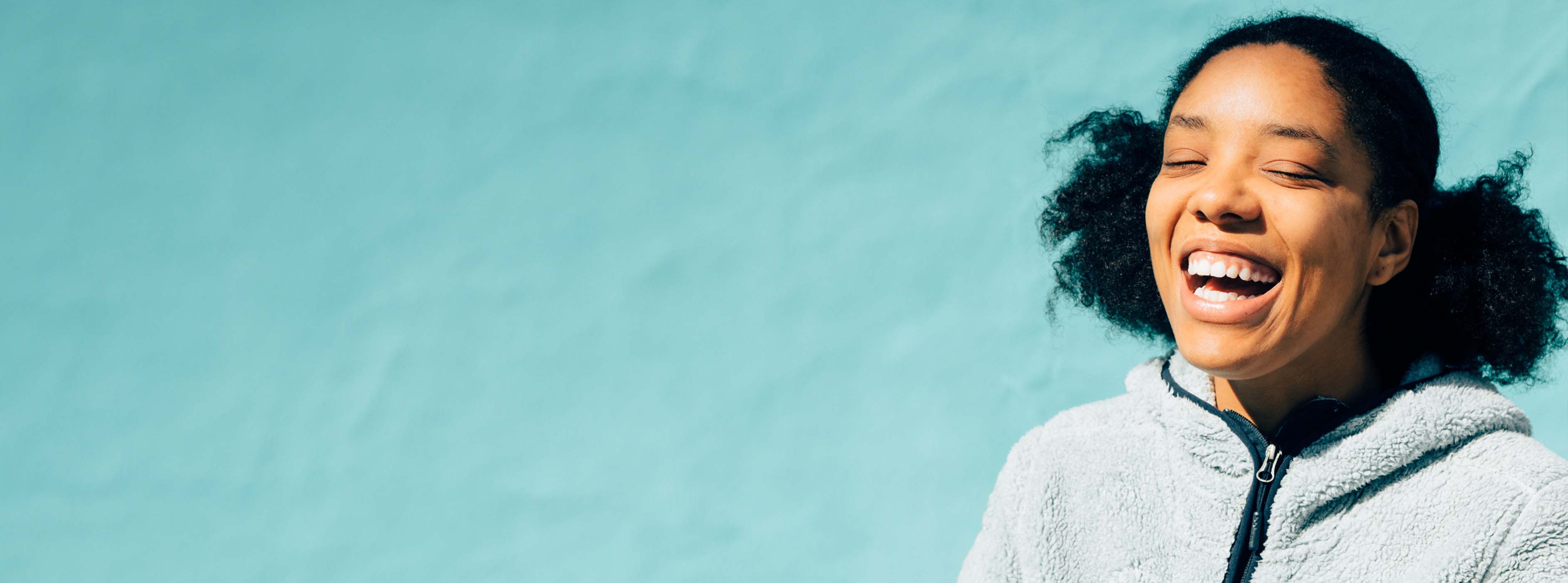 Image of a woman laughing in front of a blue wall.