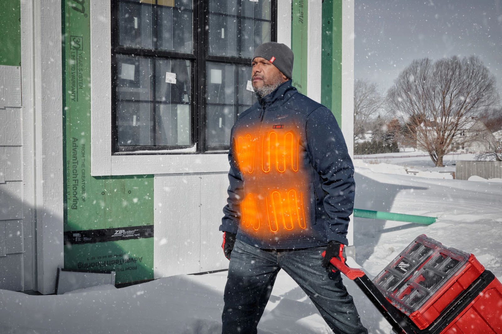 A man in a Milwaukee Heated jacket walking in the snow