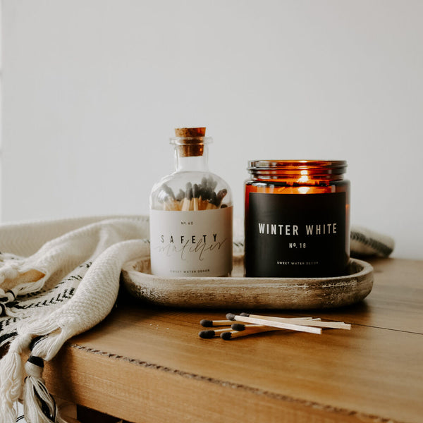 Amber jar soy candle and match bottle sitting on a rustic wood tray. 