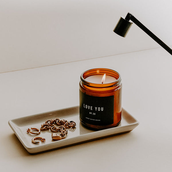 Amber jar soy candle and gold jewelry sitting on a ceramic trinket dish. 