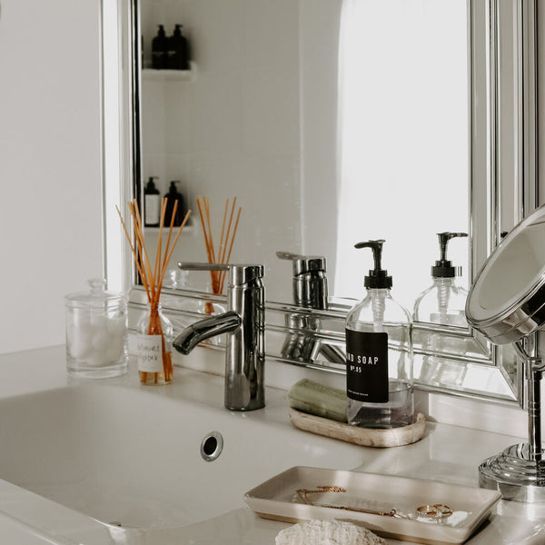 Bathroom vanity styled with a reed diffuser, refillable hand soap dispenser, and a rustic wood tray.  