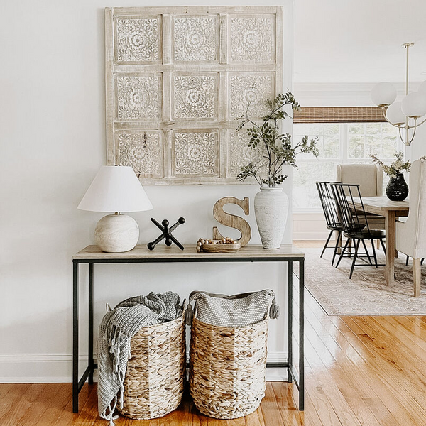 Entry table styled with a beige lamp, decorative wood try, and other neutral home decor items. 