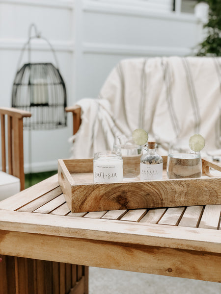 Outdoor living area with a decorative tray, soy wax candle, safety matches, and lemon water. 