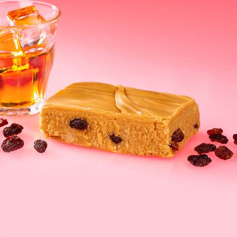 Handmade Rum and Raisin Fudge with Pink Background surrounded by a glass of rum and raisins