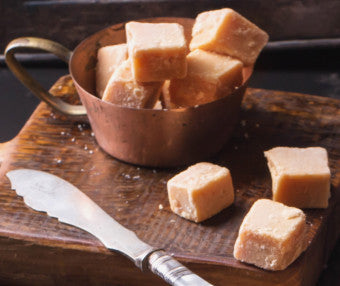 Pieces of fudge in a copper bowl on a wooden board with fudge pieces and knife