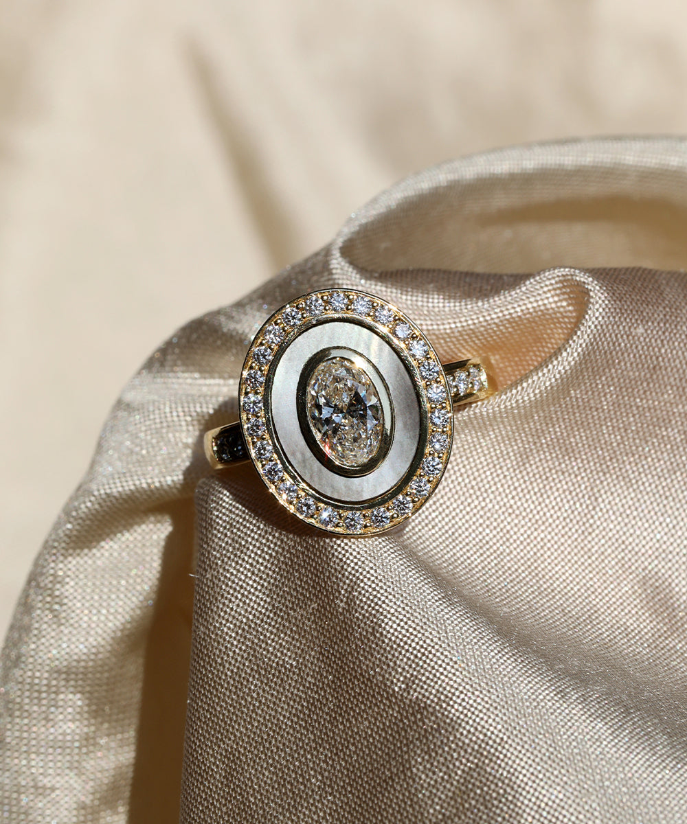 Multi layered halo bespoke engagement ring with Mother of Pearl inlay, pave diamonds and an oval cut diamond at its centre.