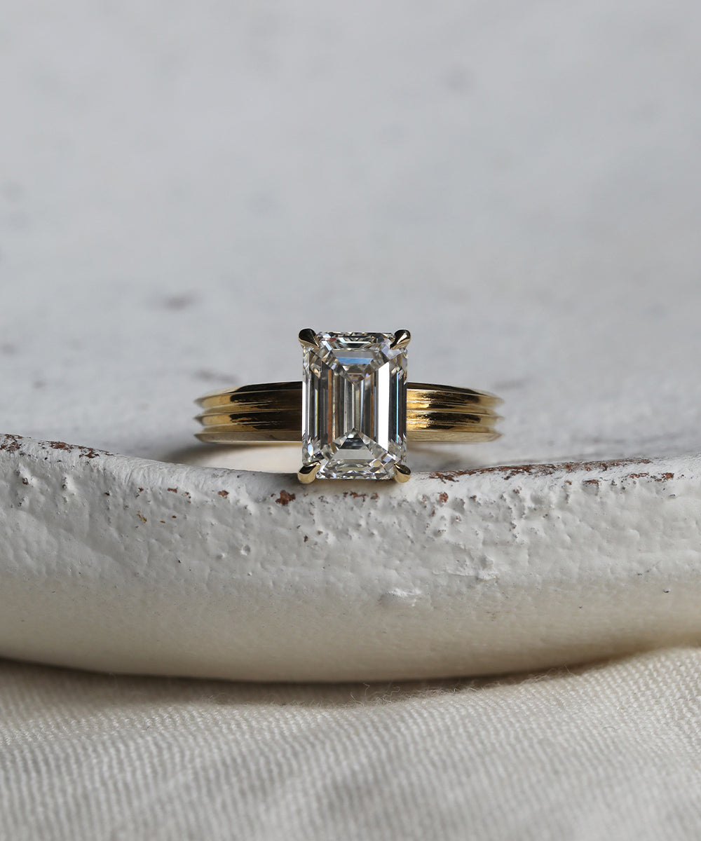 Four claw emerald cut diamond engagement ring with a statement triple knife edge band in 18ct yellow gold.