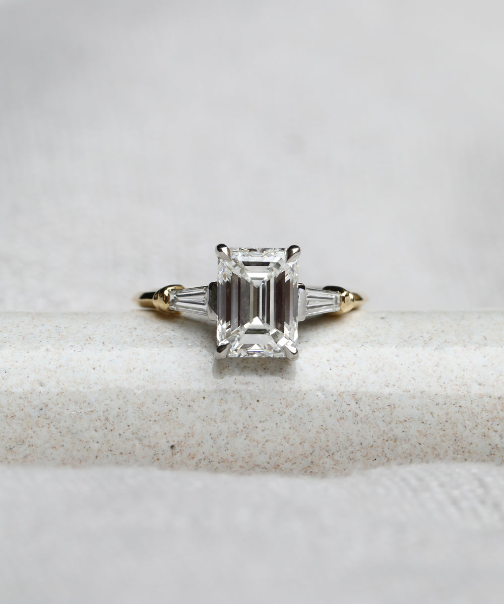 Emerald cut diamond engagement ring with tapered baguette cut diamonds either side creates a unique vintage feel to the engagement ring.