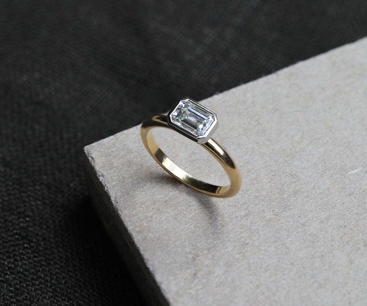 East-west set emerald cut alternative engagement ring with a split platinum setting and 18ct yellow gold band