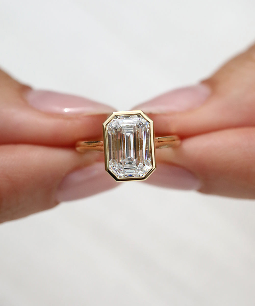Breathtaking 3ct natural emerald cut diamond engagement ring with a sleek bezel rubover setting.