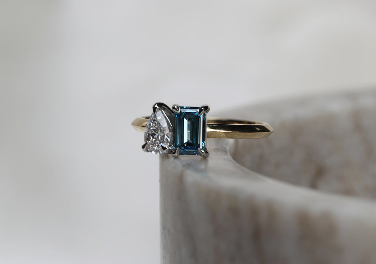 Bespoke Toi et Moi engagement ring featuring a Lab Grown fancy blue emerald cut diamond with an heirloom pear cut diamond, both with their own unique personality and beauty. We can source any of these diamonds for our clients to use in their bespoke engagement ring, or piece of fine jewellery. Handcrafted from start to finish in the UK, and designed in East London by award-winning jewellery designer Rachel Boston.