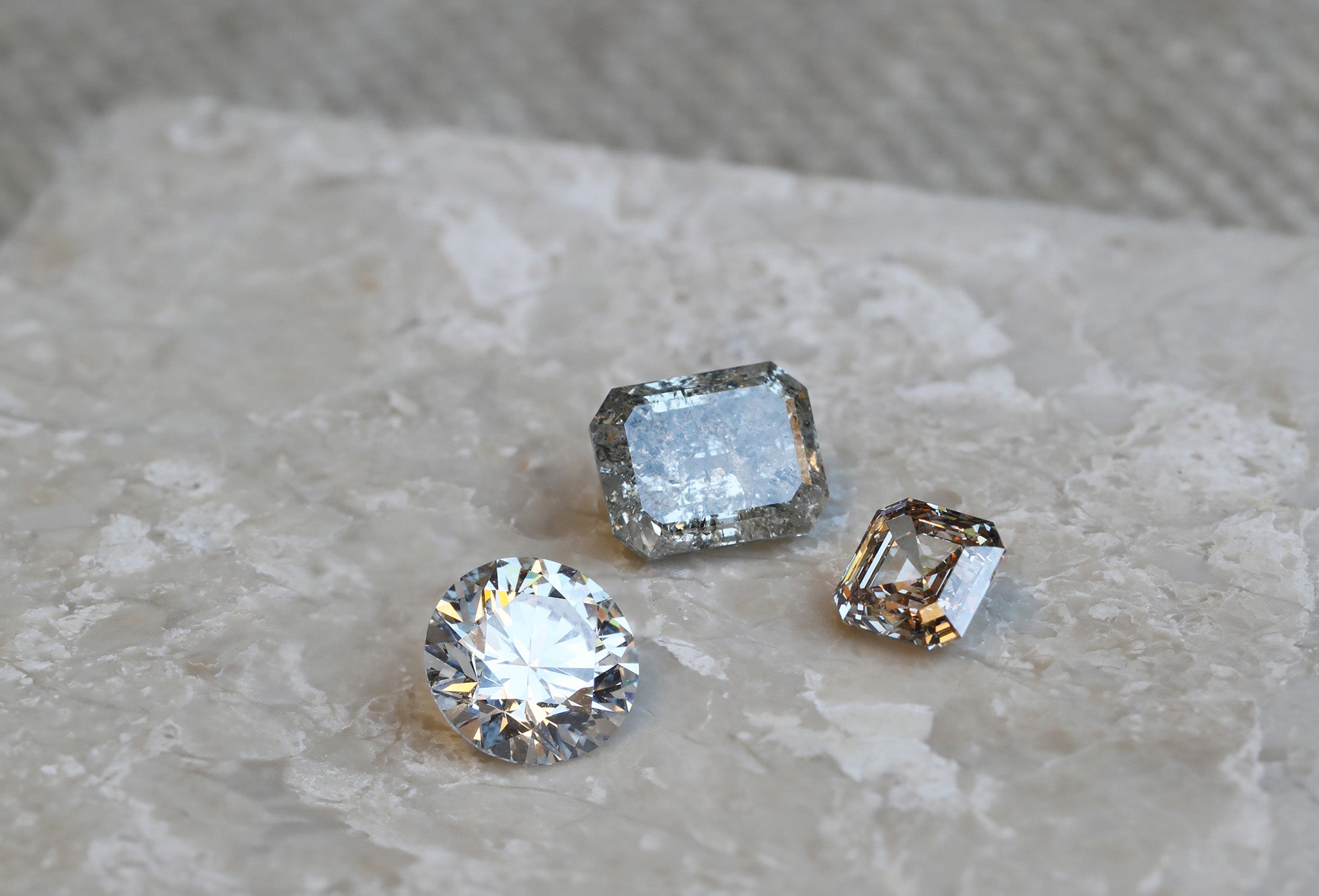 A Round Brilliant Cut diamond, Emerald Cut grey diamond and Asscher Cut Champagne diamond waiting to be turned into custom diamond engagement rings.