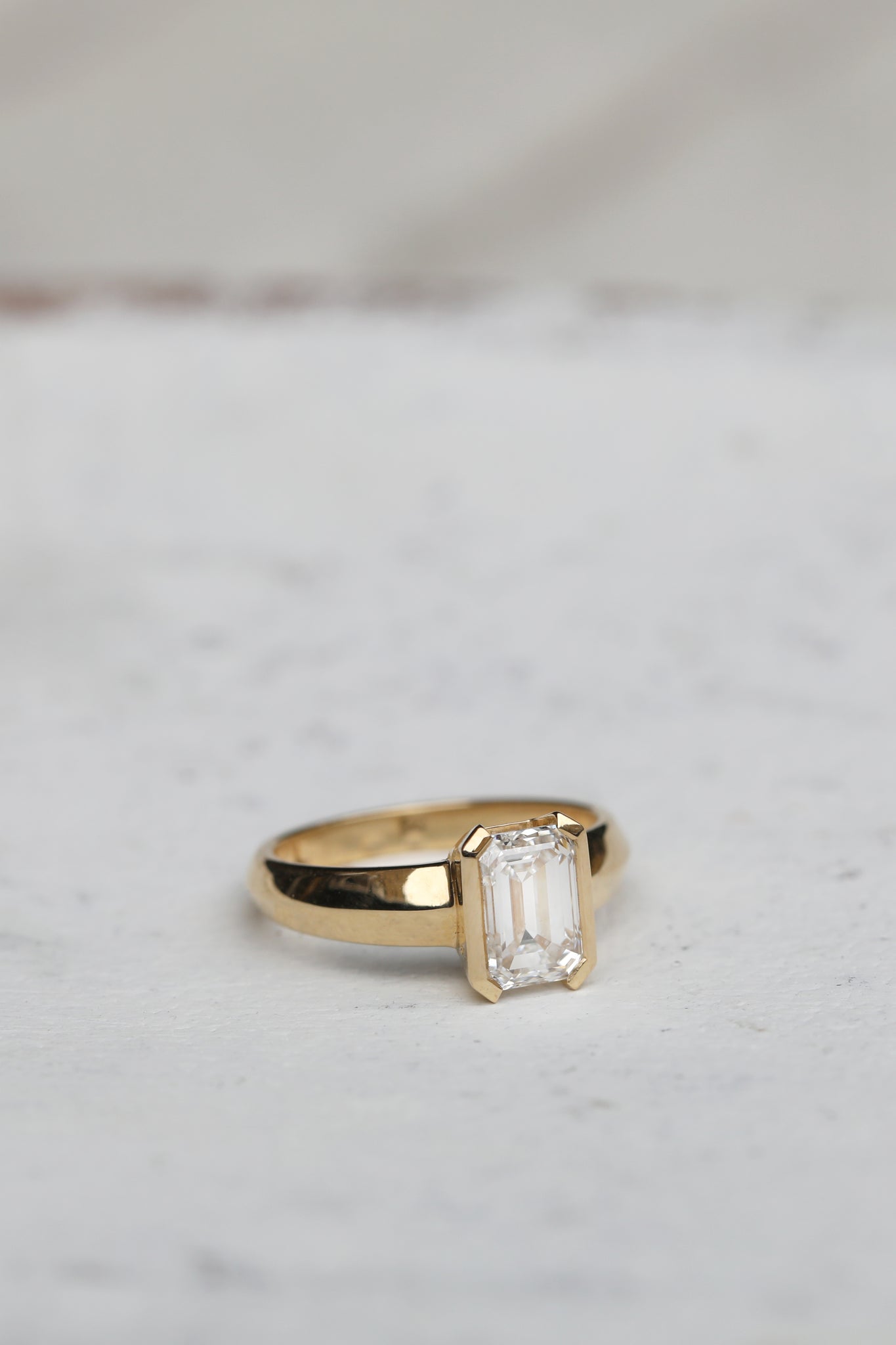 Emerald Cut Lab grown diamond for a bespoke engagement ring featuring chunky 18ct gold knife edge band and half bezel setting. Designed by East London jeweller Rachel Boston and crafted from start to finish in the UK.
