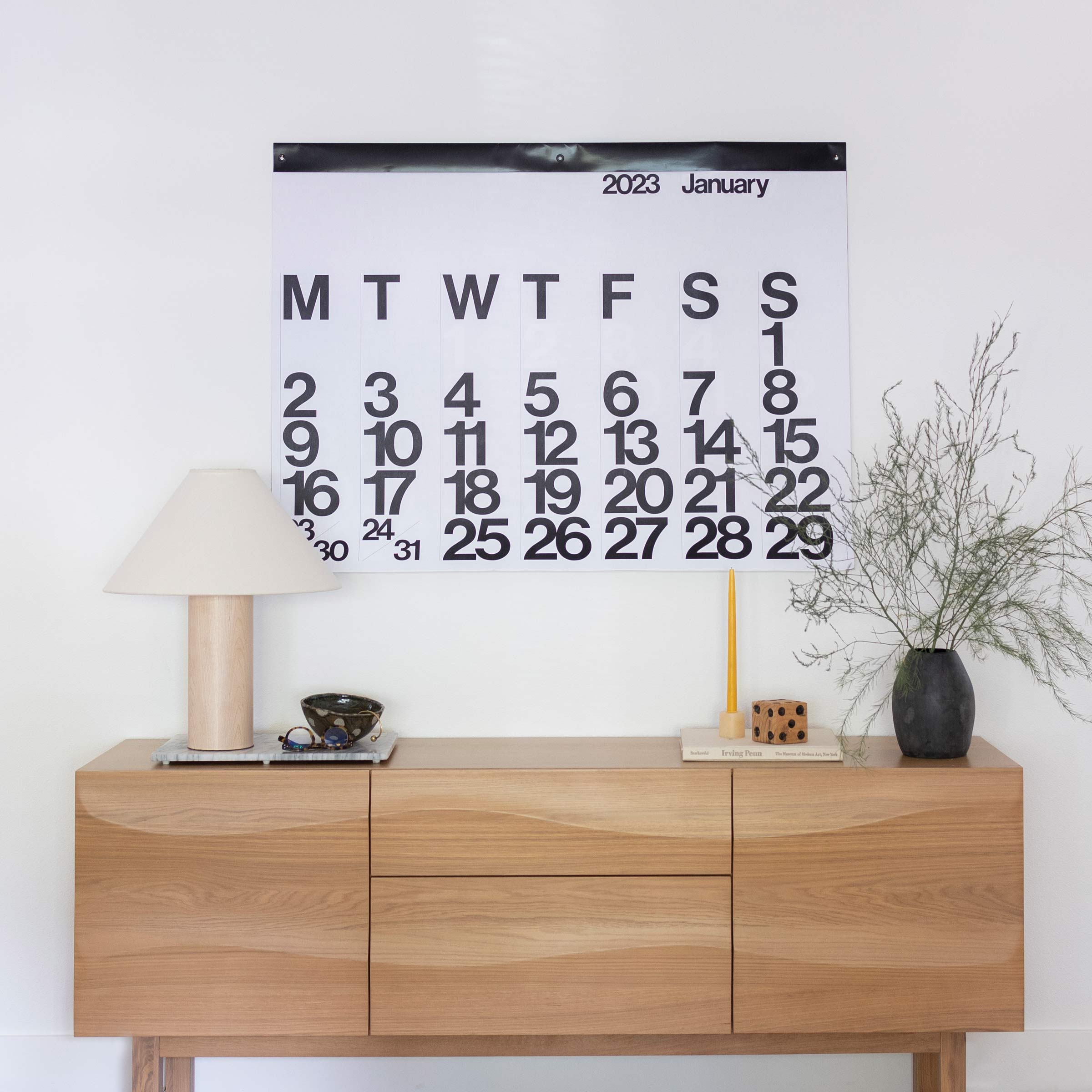 2023 Stendig Calendar hanging above a modern, wooden sideboard.