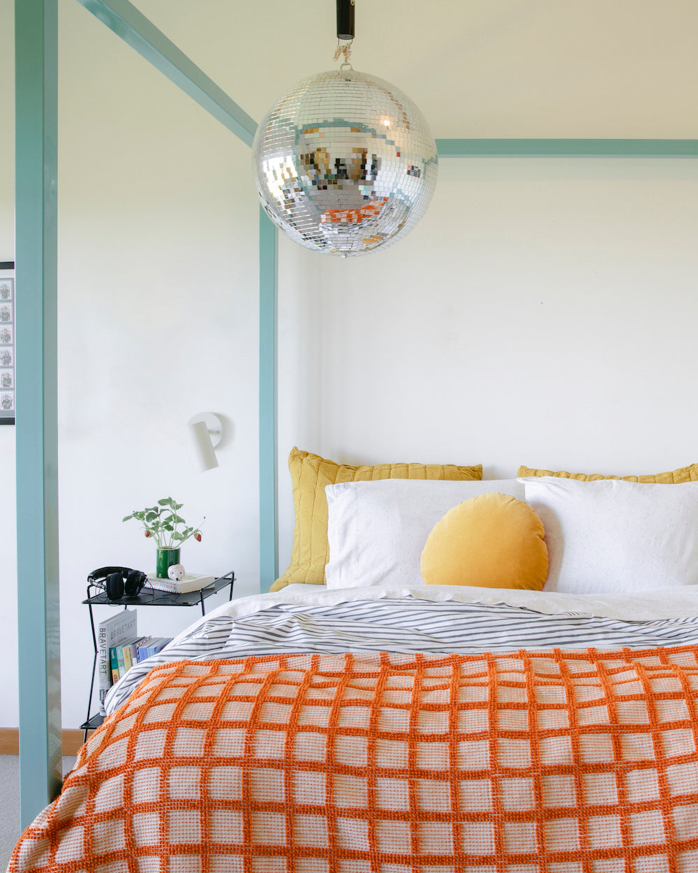 bed with a chandelier above it and a round yellow pillow on the bed and red plaid blanket