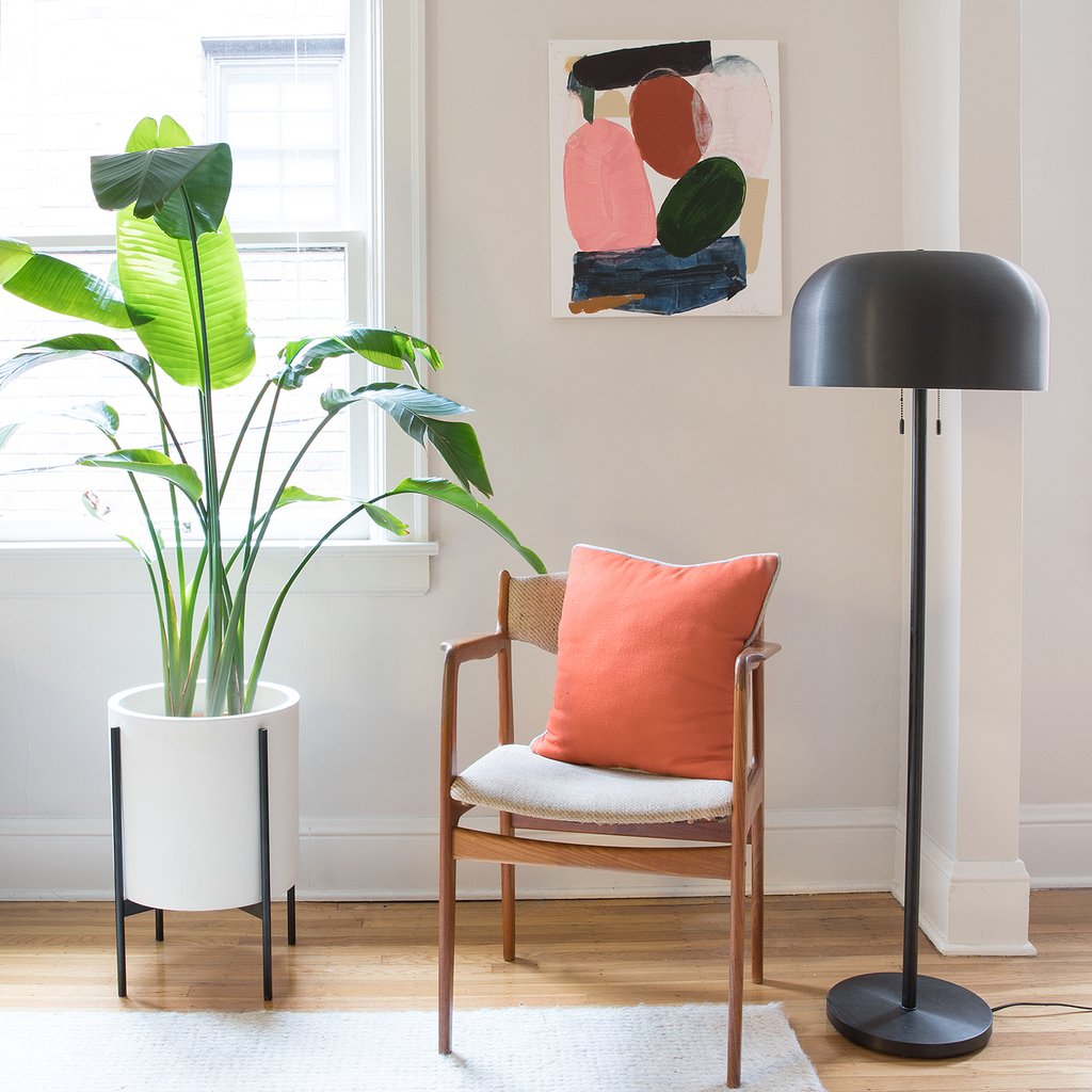 red pillow on a chair and potted plant and a black floor lamp