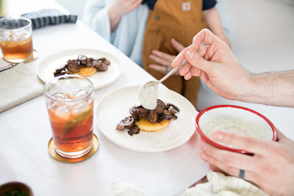 drink on a coaster and a plate of food with a person spooning a topping