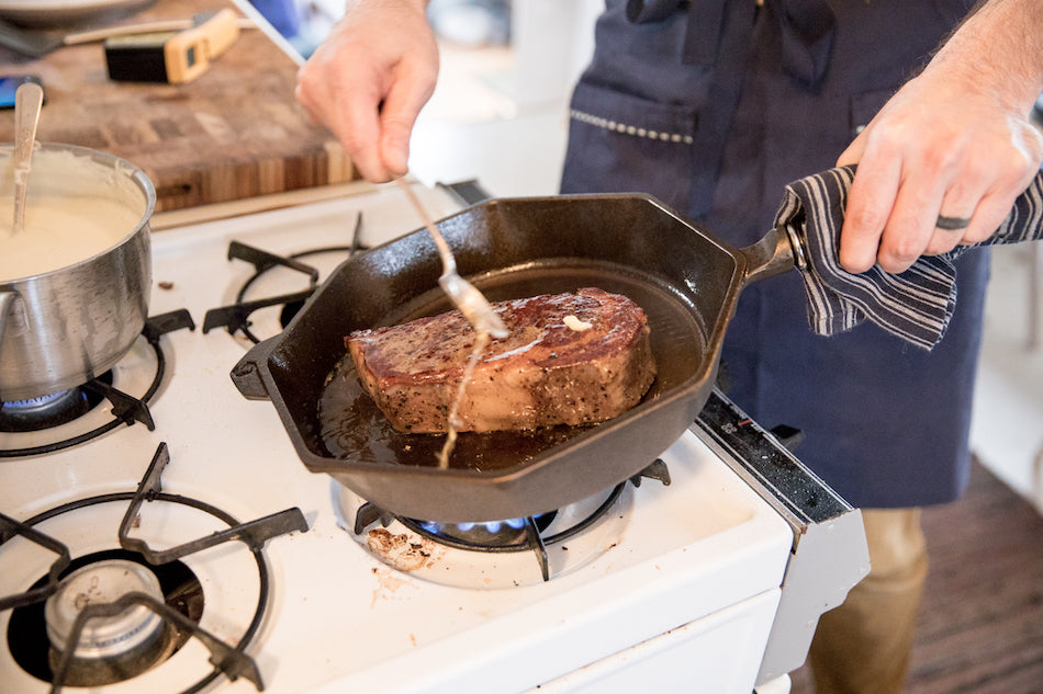 person basting a steak in pan on the stove