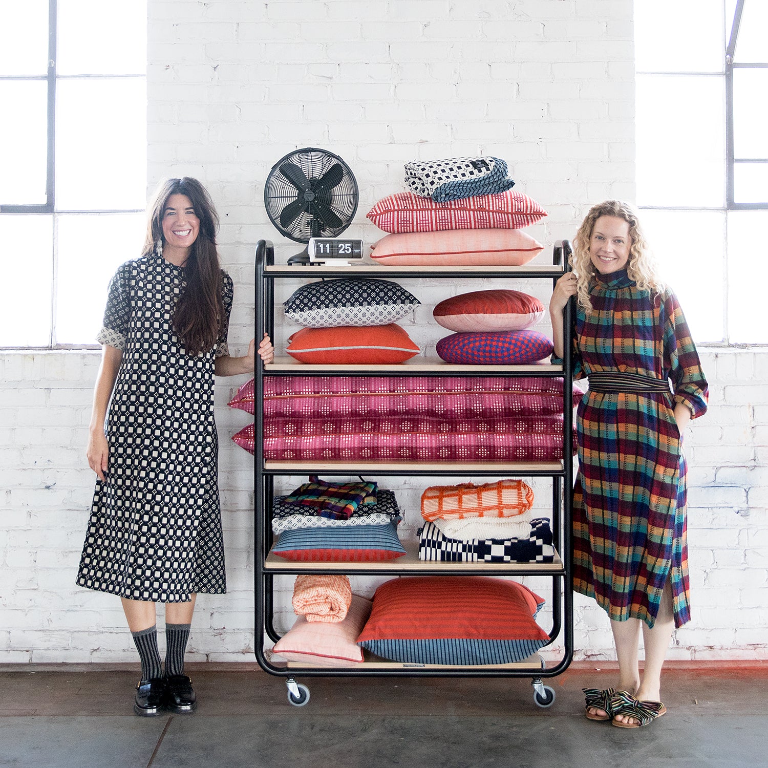 women standing next to a cart of colorful pillows