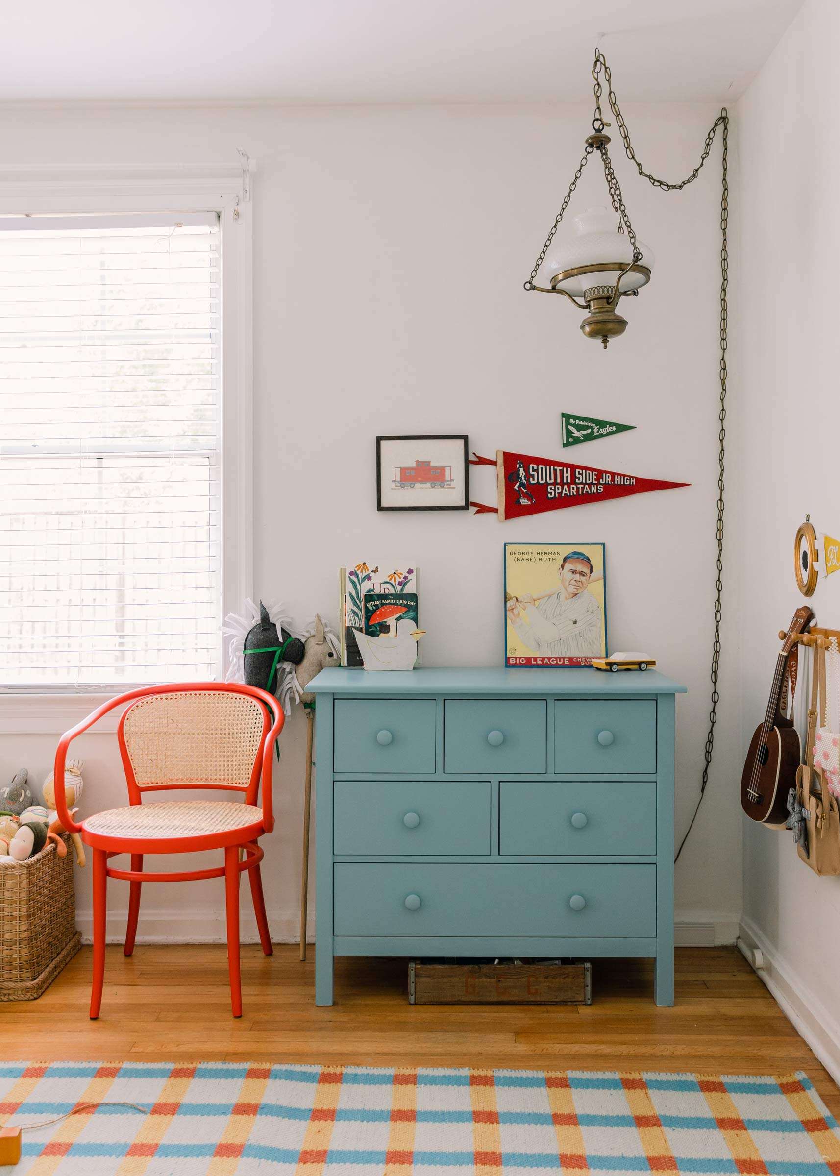 A kid's dresser with a red bentwood chair beside it. 