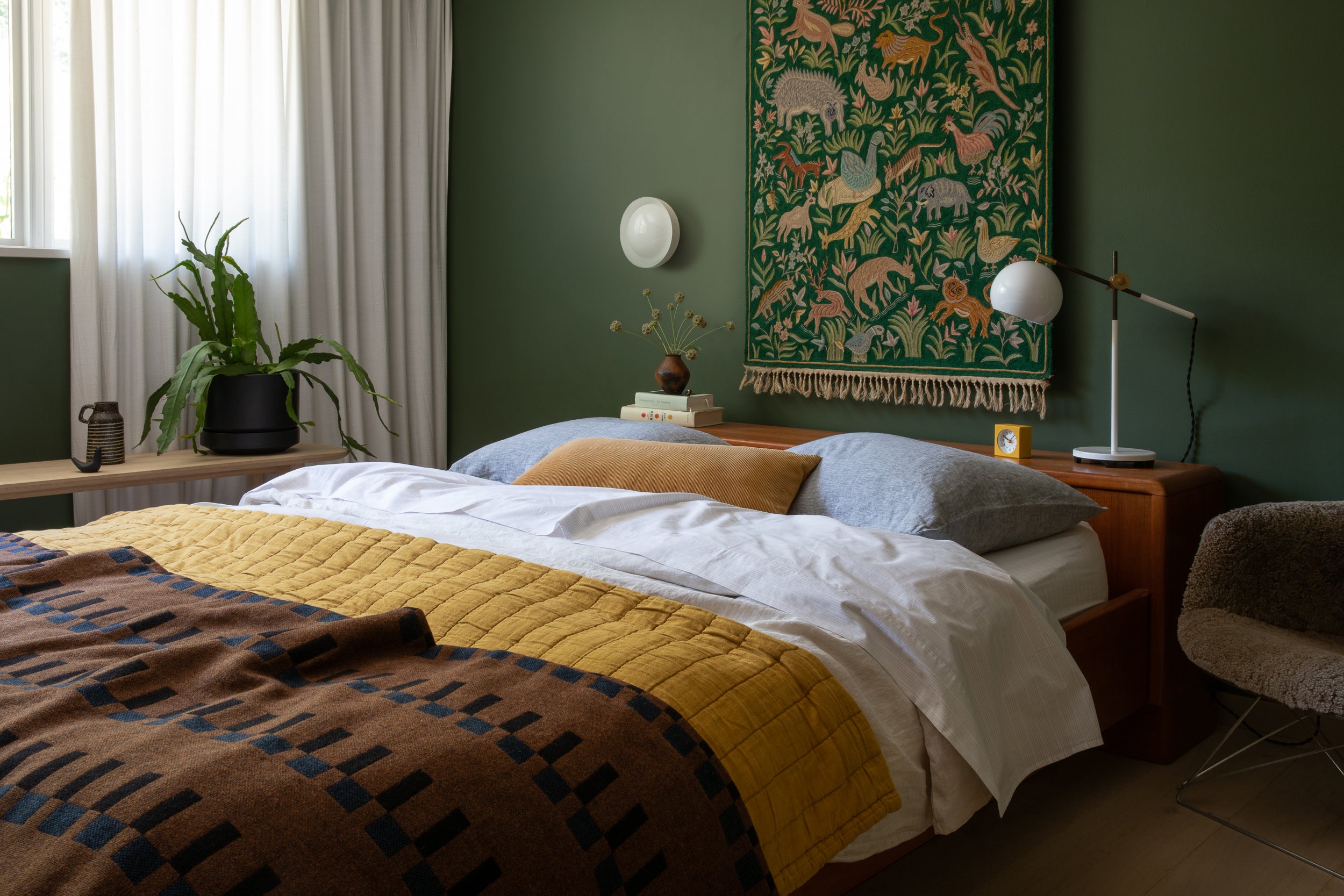 bed with a yellow blanket and a green tapestry on the wall