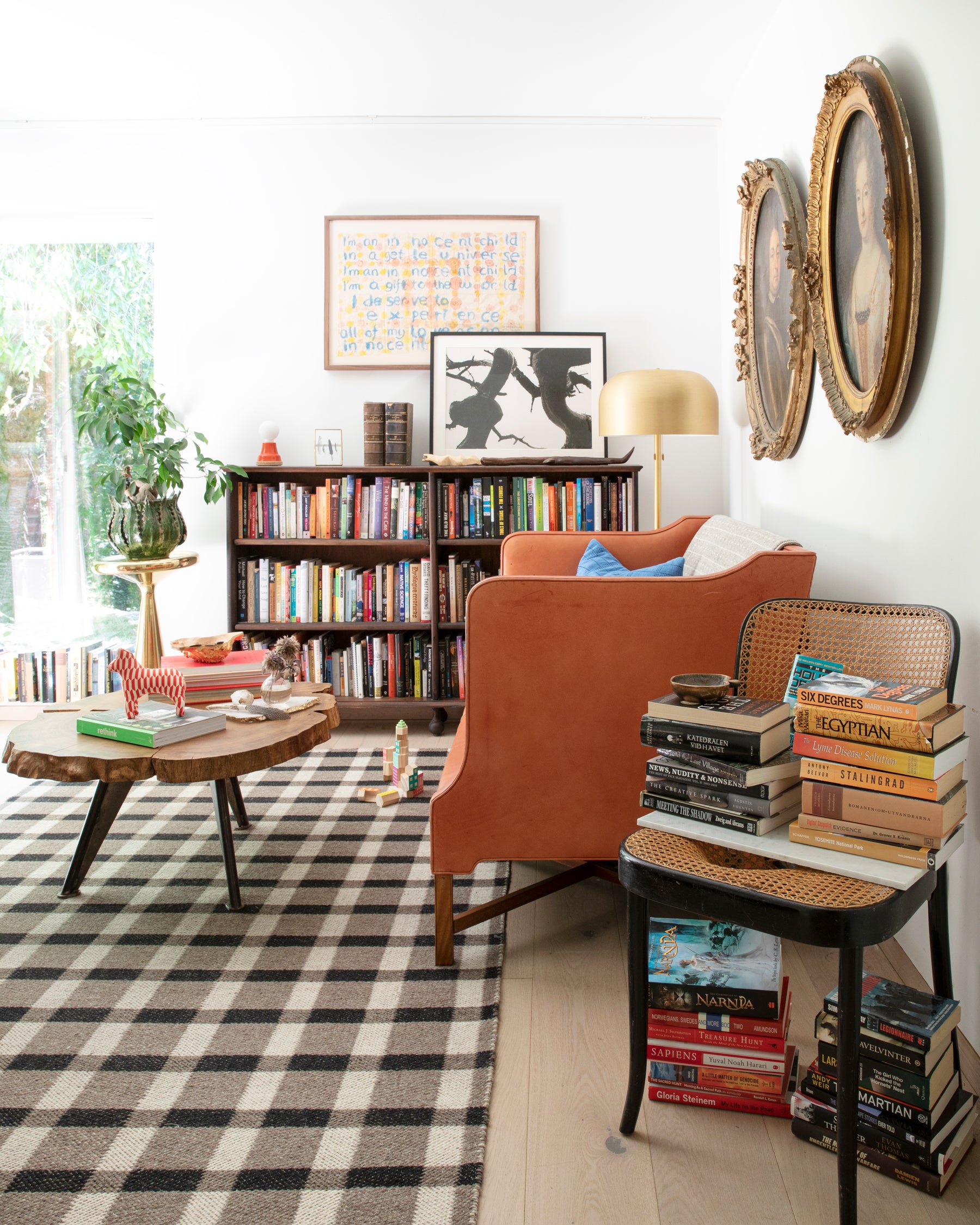 living room with a couch and a table and bookshelf filled with books and a stack of books on a chair